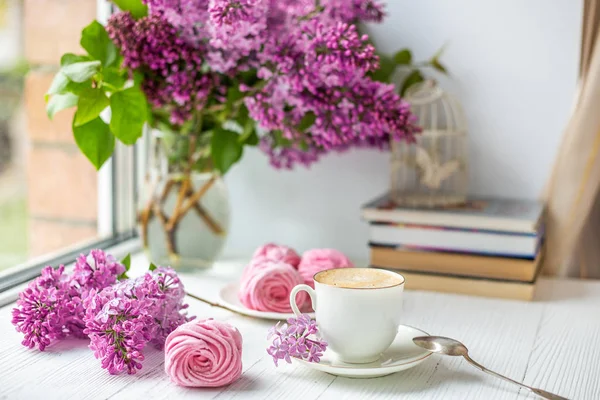 Buket leylak, fincan kahve, ev yapımı krema ve kitap yığını. Romantik bahar sabahı. Seçici odak