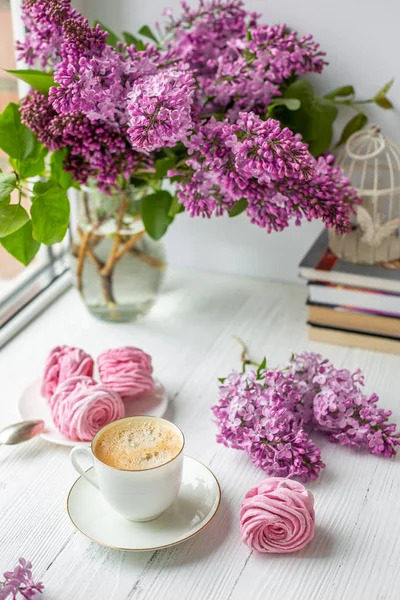 Buket leylak, fincan kahve, ev yapımı krema ve kitap yığını. Romantik bahar sabahı. Seçici odak