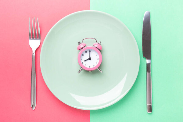 Pink alarm clock, fork, knife and empty plate on colored paper background. Intermittent fasting concept- Image