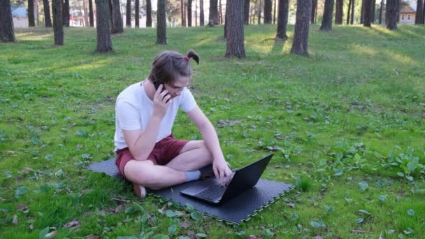 年轻人坐在草地上 停在公园里 一边工作一边用笔记本电脑 一边打电话 远程学习概念 4K镜头 — 图库视频影像