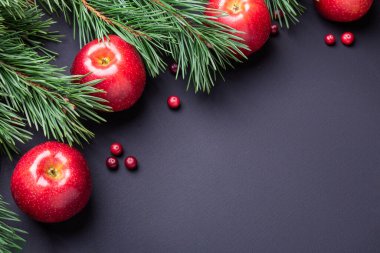 Noel kompozisyonu köknar dalları ve siyah ahşap arka planda kırmızı elmalar