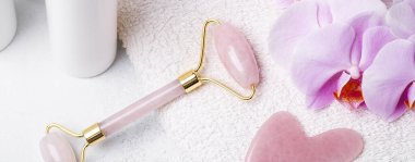 Rose Quartz Yeşim Roller, Gua Sha masaj aleti ve arkaplanda orkide çiçekli yatay pankart