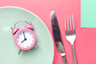 Pembe alarm saati, çatal, bıçak ve renkli kağıtta boş tabak. Aralıklı oruç kavramı - Resim