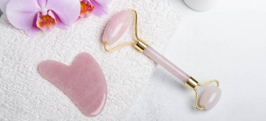 Rose Quartz Yeşim Roller, Gua Sha masaj aleti ve arka planda orkide çiçeği olan yatay afiş. Evde yüz ve vücut bakımı - Görüntü