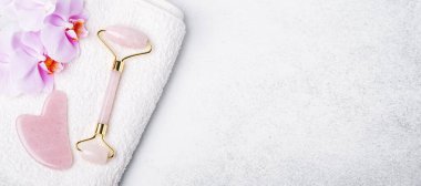 Rose Quartz Yeşim Roller, Gua Sha masaj aleti ve arkaplanda orkide çiçekli yatay pankart