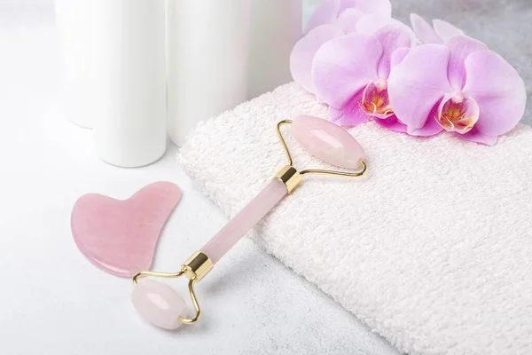 Rose Quartz jade roller and Gua Sha massager on towel on stone background. Massage tool for facial skin care, SPA beauty treatment concept - Image