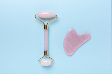 Gua Sha masaj aleti ve mavi arka planda yüz silindiri. Yüz bakımı için masaj aleti, SPA güzellik tedavisi konsepti. Yatay Pankart - Resim