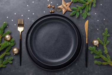 Boş siyah seramik tabağı, köknar ağacı dalı ve siyah taş zemin üzerinde altın aksesuarları olan bir Noel masası. Üst Manzara. Uzayı kopyala - Resim