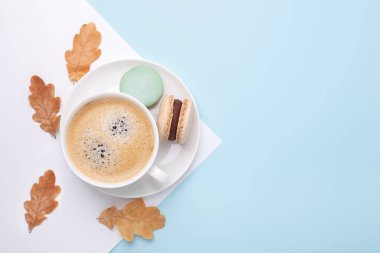 Yaratıcı sonbahar yatağı. Mavi arka planda bir fincan kahve, badem kurabiyesi ve meşe yaprağı.