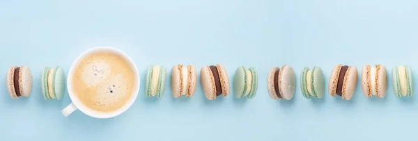 Creative flat lay. Cup of coffee, various macarons on blue background. Long horizontal banner - Image