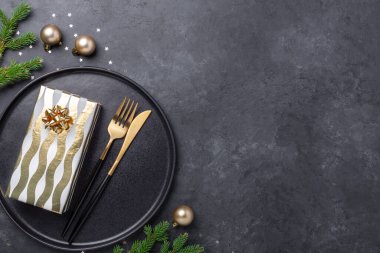Siyah seramik tabağı, hediye kutusu ve siyah taş arka planda altın aksesuarları olan bir Noel masası. Metnin için alanı kopyala - Resim