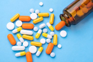 Mavi arka plandaki cam şişeden dökülen bir yığın hap ve kapsül. Yakın plan - Görüntü