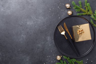 Noel sofrası. Altın hediye kutusu olan siyah seramik tabak, köknar ağacı dalı ve taş zemin üzerinde aksesuarlar. Altın Madalya - Resim