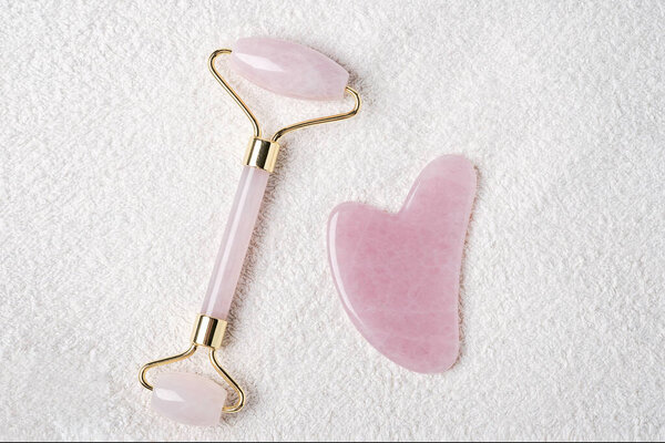 Rose quartz jade roller and Gua Sha massaging tool on towel. Anti age, lifting and toning treatment at home. Top view - Image