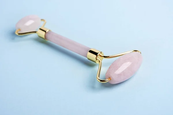 Rose Quartz jade roller on blue background. Massage tool for facial skin care, SPA beauty treatment concept - Image