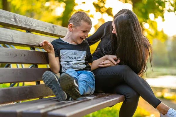 Mom Tickles Her Son on a Park Benck  in Autum with Colorful Backgroun in a Sunny Day, Both Laughing- Caption on Shirt \