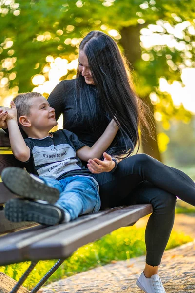 Mom Tickles Her Son on a Park Benck  in Autum with Colorful Backgroun in a Sunny Day, Both Laughing- Caption on Shirt \