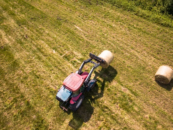 用红色拖拉机在麦田里收获干草卷的空中无人机照片 阳光明媚的夏日 — 图库照片