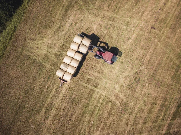 Aerial Drone Photo of Farmer Harvesting Hay Rolls in the Wheat Field with a Red Tractor - Sunny Summer Day, Vintage Look Edit