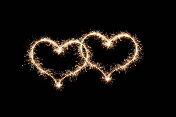 两颗心是黑色背景上的火花所创造的爱情象征 — 图库照片