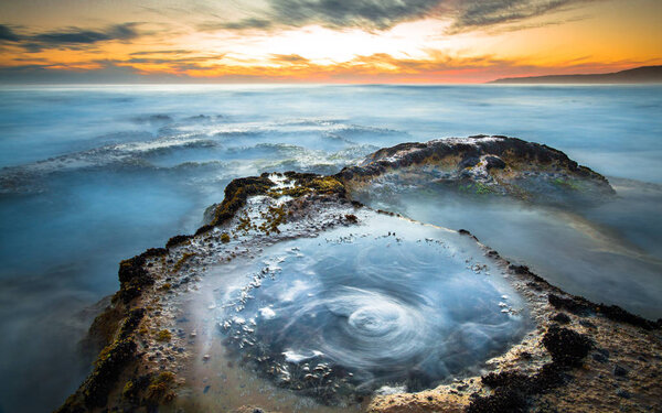 Long exposure of ocean waves flowing over rocky tidepools at sunset on Johanna Beach in the Great Otway National Park, Victoria, Australia.
