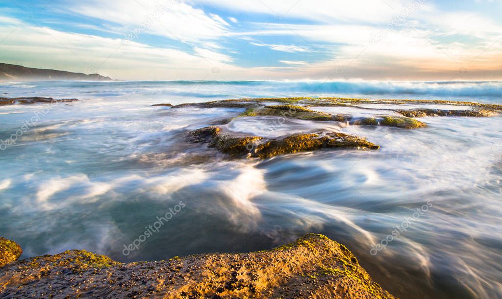 Long exposure of ocean waves flowing over rocky tidepools at sunset on Johanna Beach in the Great Otway National Park, Victoria, Australia.