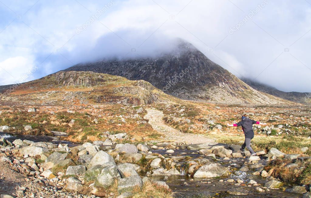 A hiker jumps on rocks to cross a stream in the Mourne Mountains, UK