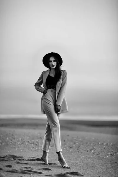 Atraktivní dívka v obleku a klobouk na pláži při západu slunce — Stock fotografie