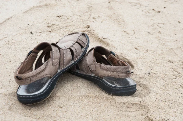Leather sandals on the sand of the beach with light sifted on cloudy day Royalty Free Stock Images
