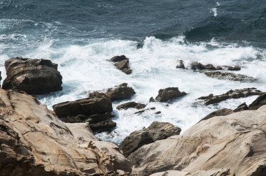 Arka planda kayalar ve onlara karşı dayak dalgaları ile Cliff