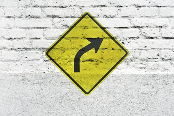 Traffic board signaling curve to the right stamped on white brick wall, like a graffiti