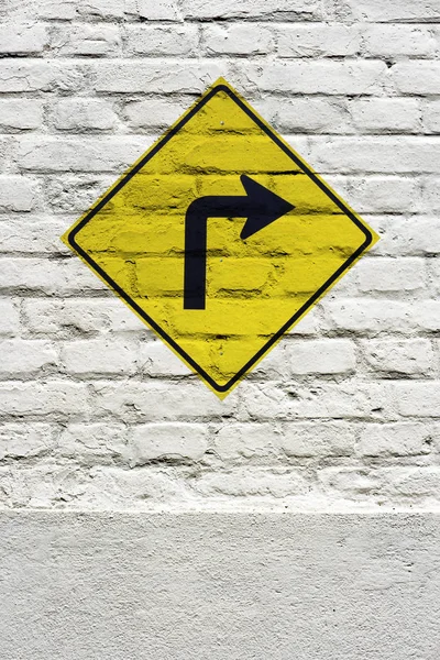 Traffic board signaling curve to the right stamped on white brick wall, like a graffiti