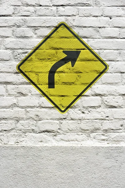 Traffic board signaling curve to the right stamped on white brick wall, like a graffiti