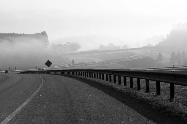 Highway in perspective, with guard rail highlighted and morning fog in the background