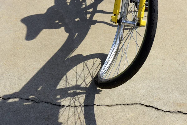 Close-up of crooked bicycle wheel, projecting surreal shadow on sidewalk