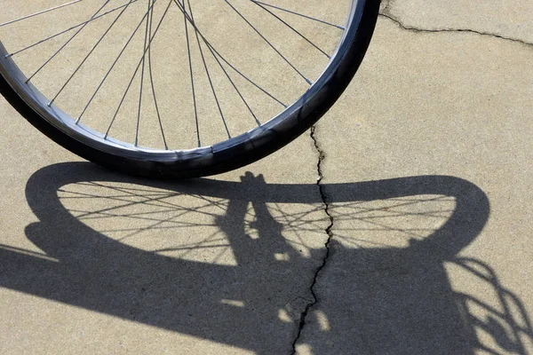 Close-up of crooked bicycle wheel, projecting surreal shadow on sidewalk