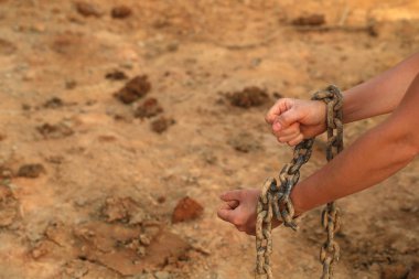 human hands in old rusty chains against sandy beach clipart