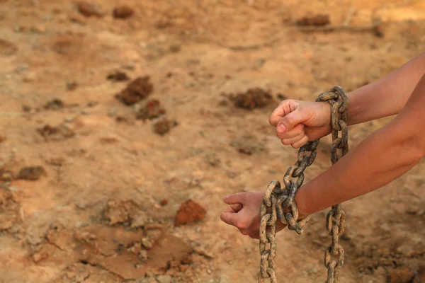 human hands in old rusty chains against sandy beach