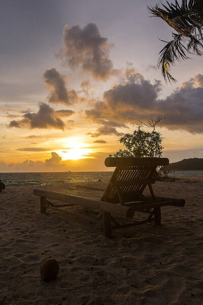 Wooden chaise lounge on sandy beach during sunset