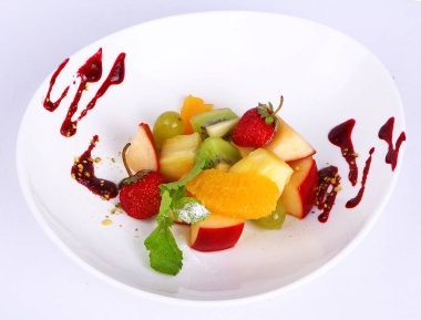 Fresh fruit salad with various tasty ingredients and sauce on white plate.