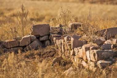 dry grass in rural field with stacked stones, autumnal landscape background.