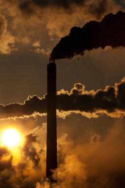sunset with industrial chimney with smoke clouds over bright sunlight in evening sky