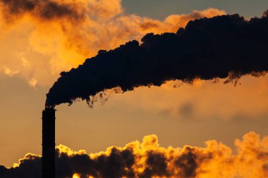 sunset scenery with industrial chimney with smoke clouds over bright sunlight in evening sky