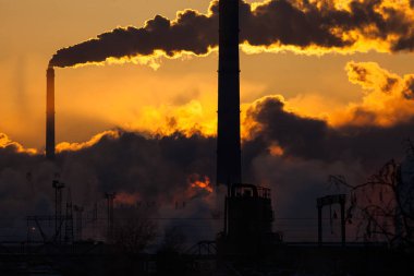 Elektrik santrali ve bacaların silueti gün batımında sisli bulutlarda boğuluyor..
