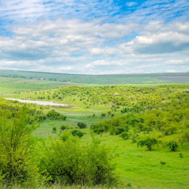 Nehri Vadisi tepeler ve teraslar ile. Yamaçlarda çalılar, ağaçlar ve otlar büyür. Cumulus bulutları mavi gökyüzünde ışık.