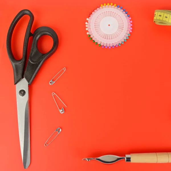 Tailoring scissors and pins on a red background. Flat lay, top view. Free space for text.