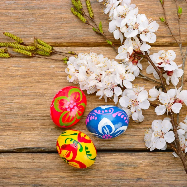 Uova di Pasqua e un rametto di albicocca in fiore sul backgrou di legno — Foto Stock