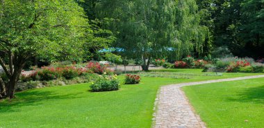 Manikürlü çimleri ve renkli çiçek tarlaları olan sakin bir parkın içinden geçen büyüleyici bir kaldırım taşı yolu. Bu görüntü huzur ve güzel bir günde sakin bir gezinti hissi uyandırıyor..