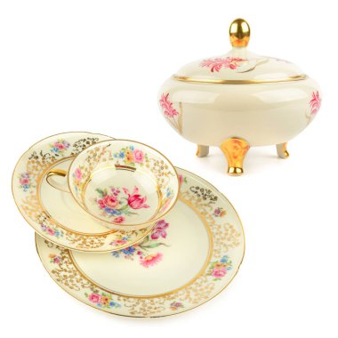 An elegant vintage porcelain tea set, including a tea cup, saucer, plate, and covered bowl, is beautifully decorated with a floral pattern and gold trim. The items are isolated on a white background, highlighting their intricate design.