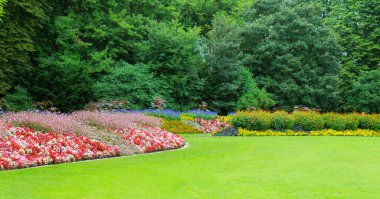 A large expanse of perfectly manicured green lawn leads to a beautifully arranged, curved flower bed filled with a variety of colorful blooms. The scene conveys a sense of tranquility, nature's beauty, and meticulous gardening.